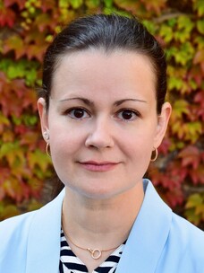 Yana Vaynzof mit zusammengebundenem Haar, vor herbstlichem Hintergrund.